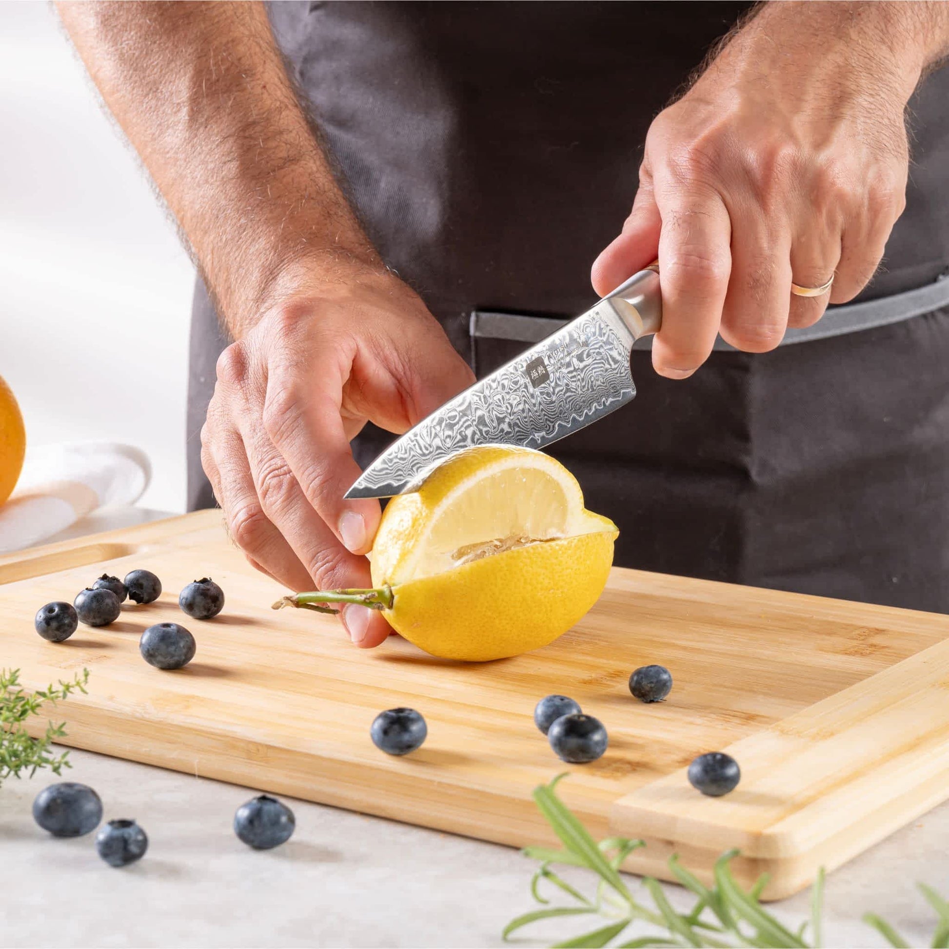 Eine Person schneidet mit dem Kyotsu Allzweckmesser aus Damaststahl eine Zitrone auf einem Holz-Schneidebrett – hochwertiges Messer in Aktion.