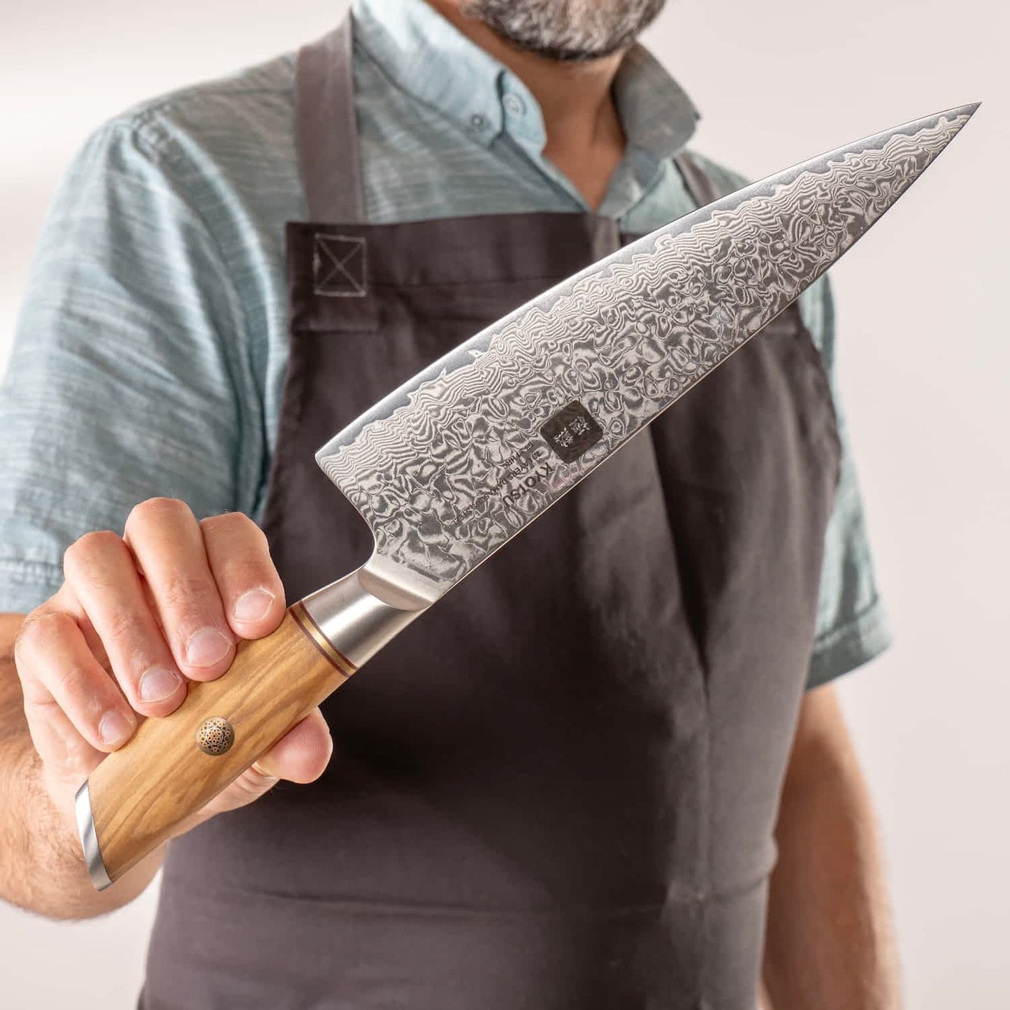 Person mit Schürze präsentiert Kyotsu Chefmesser aus Damaststahl.