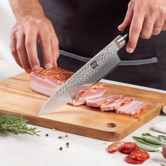Eine Person schneidet mit dem Kyotsu Chefmesser aus Damaststahl Fleisch auf einem Holz-Schneidebrett – hochwertiges Messer in Aktion.