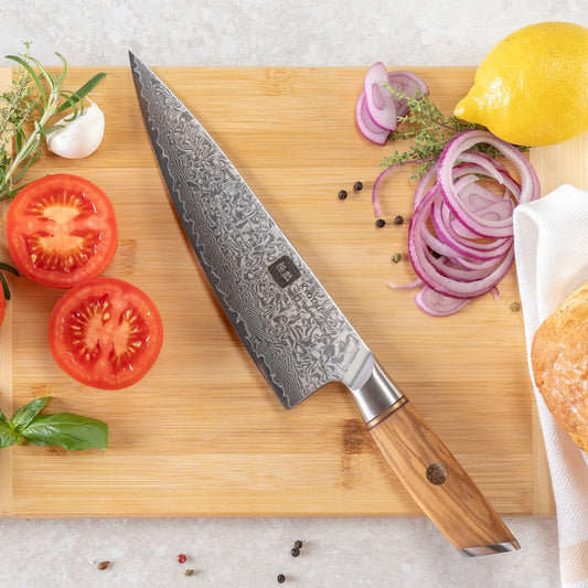Kyotsu Chefmesser aus Damaststahl auf Holz-Schneidebrett mit frischen Zutaten – stilvolle Produktpräsentation für hochwertige Küchenmesser.