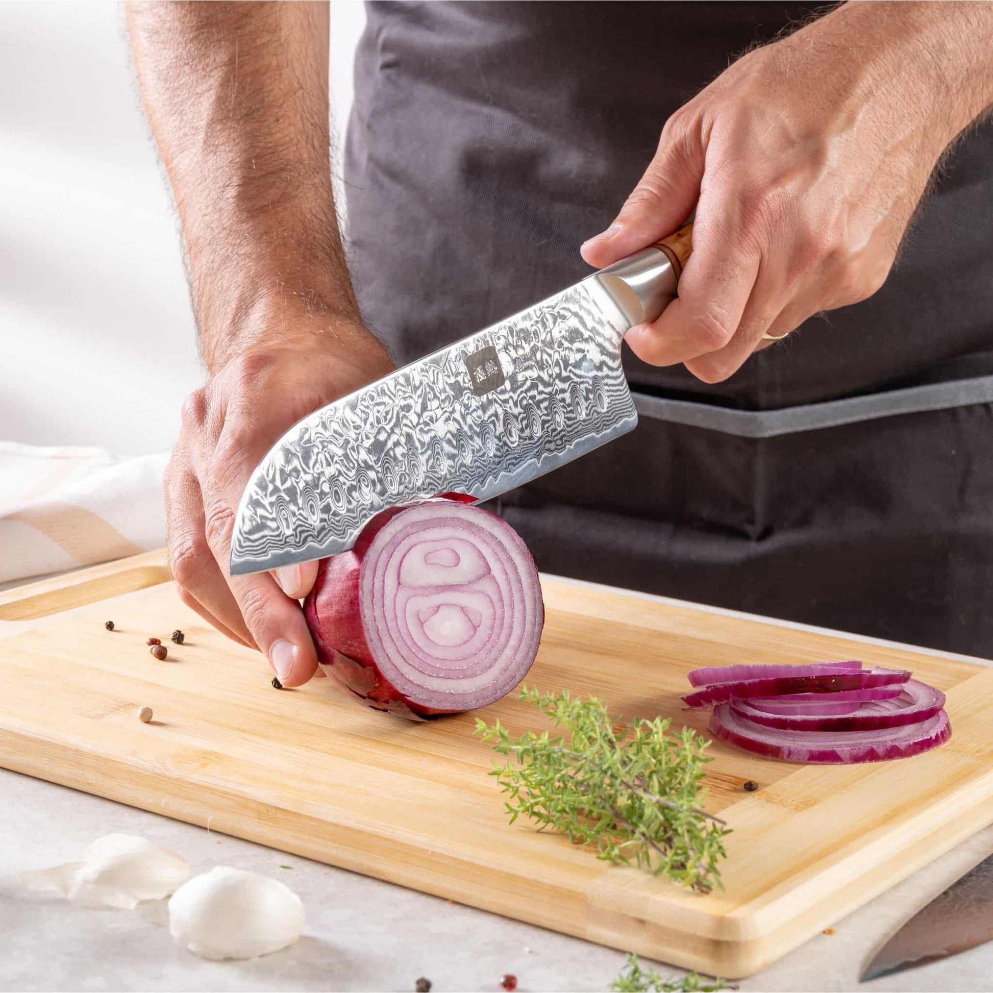 Eine Person schneidet mit dem Kyotsu Santoku-Messer aus Damaststahl Zwiebeln auf einem Holz-Schneidebrett – hochwertiges Messer in Aktion.