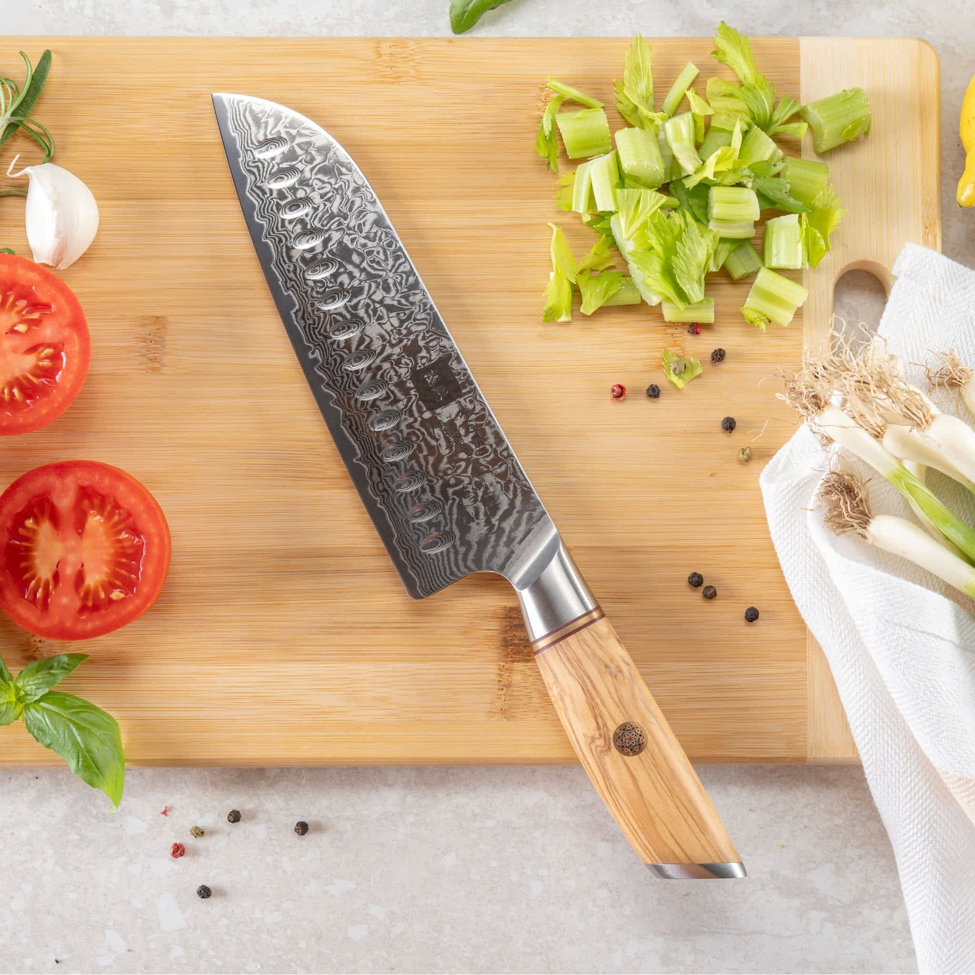 Kyotsu Santoku-Messer aus Damaststahl auf Holz-Schneidebrett mit frischen Zutaten – stilvolle Produktpräsentation für hochwertige Küchenmesser.