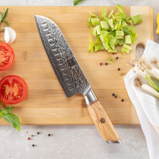 Kyotsu Santoku-Messer aus Damaststahl auf Holz-Schneidebrett mit frischen Zutaten – stilvolle Produktpräsentation für hochwertige Küchenmesser.