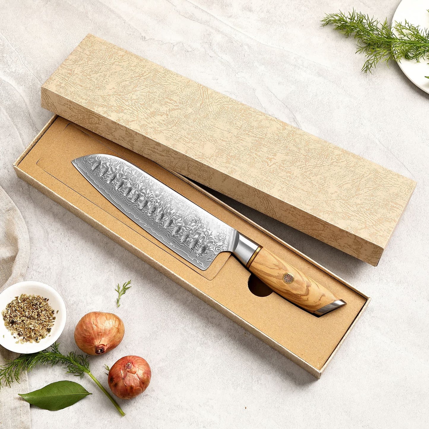 Kyotsu Santoku-Messer aus Damaststahl in geöffneter Verpackung – daneben Deckel und frische Zutaten.