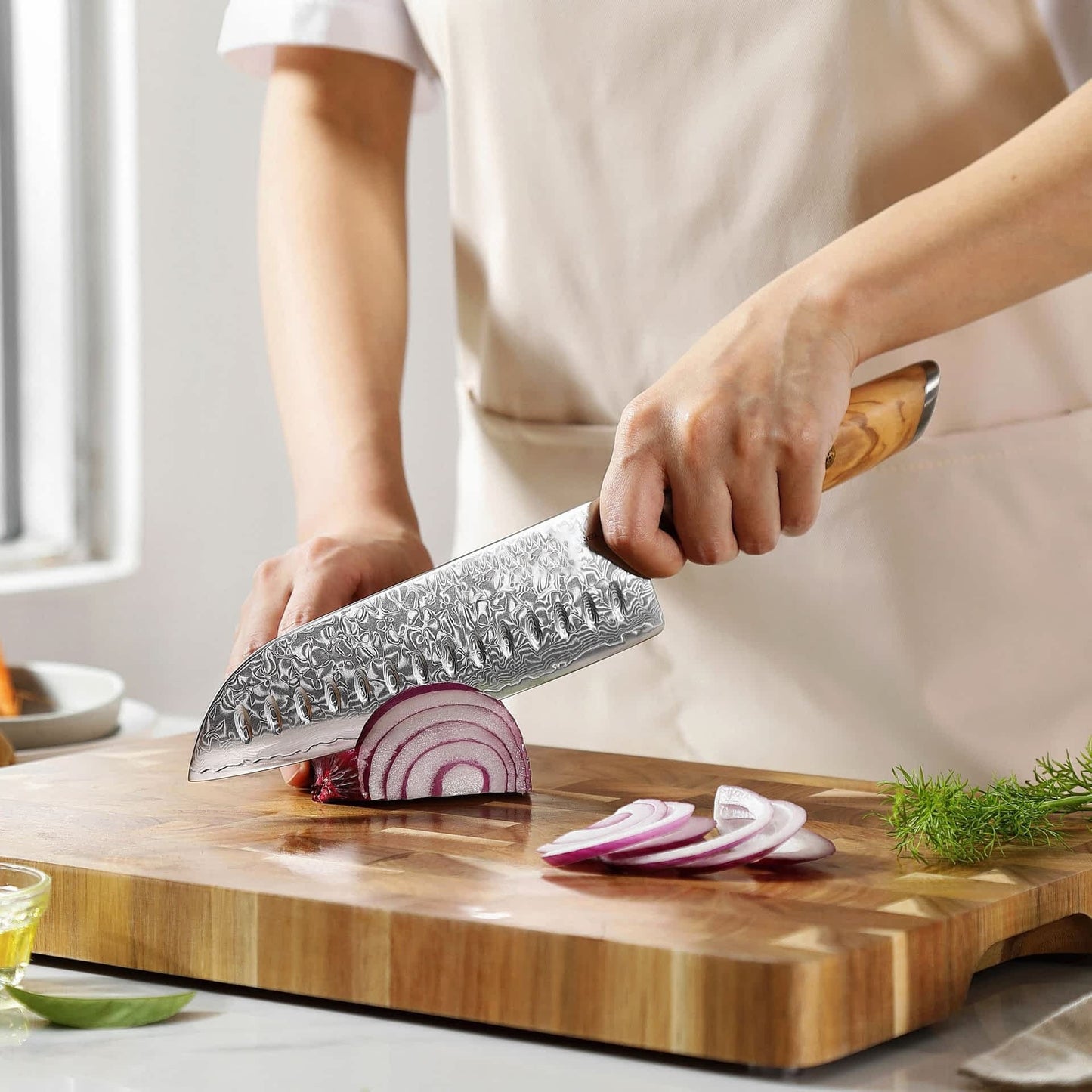 Eine Person schneidet mit dem Kyotsu Santoku-Messer aus Damaststahl Zwiebeln auf einem Holz-Schneidebrett – hochwertiges Messer in Aktion.