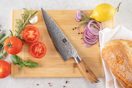 Kyotsu Chefmesser aus Damaststahl auf Holz-Schneidebrett mit frischen Zutaten – stilvolle Produktpräsentation für hochwertige Küchenmesser.