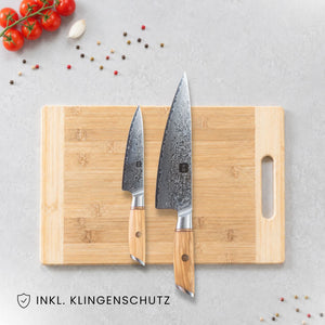 Kyotsu 2er-Set Olive: Allzweckmesser und Chefmesser liegen auf einem Holz-Schneidebrett, daneben frische Zutaten.