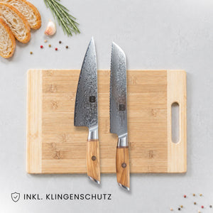 Kyotsu 2er-Set Olive: Chefmesser und Brotmesser liegen auf einem Holz-Schneidebrett, daneben frische Zutaten.