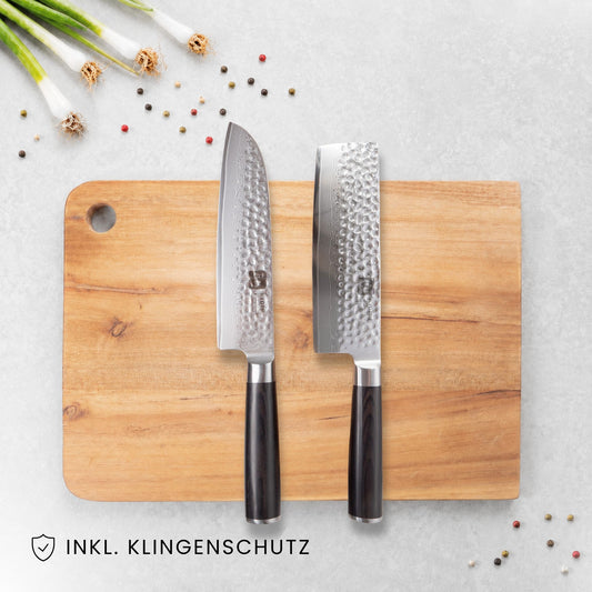 Kyotsu 2er-Set Pakka: Santoku-Messer und Nakiri-Messer liegen auf einem Holz-Schneidebrett, daneben frische Zutaten.