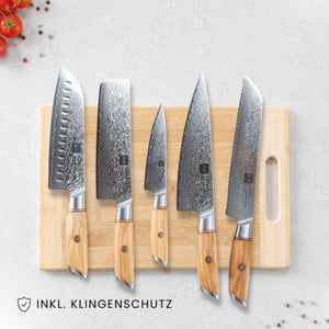 Kyotsu 5er-Set Olive: Santoku-Messer, Nakiri-Messer, Allzweckmesser, Chefmesser und Brotmesser liegen auf einem Holz-Schneidebrett, daneben frische Zutaten.