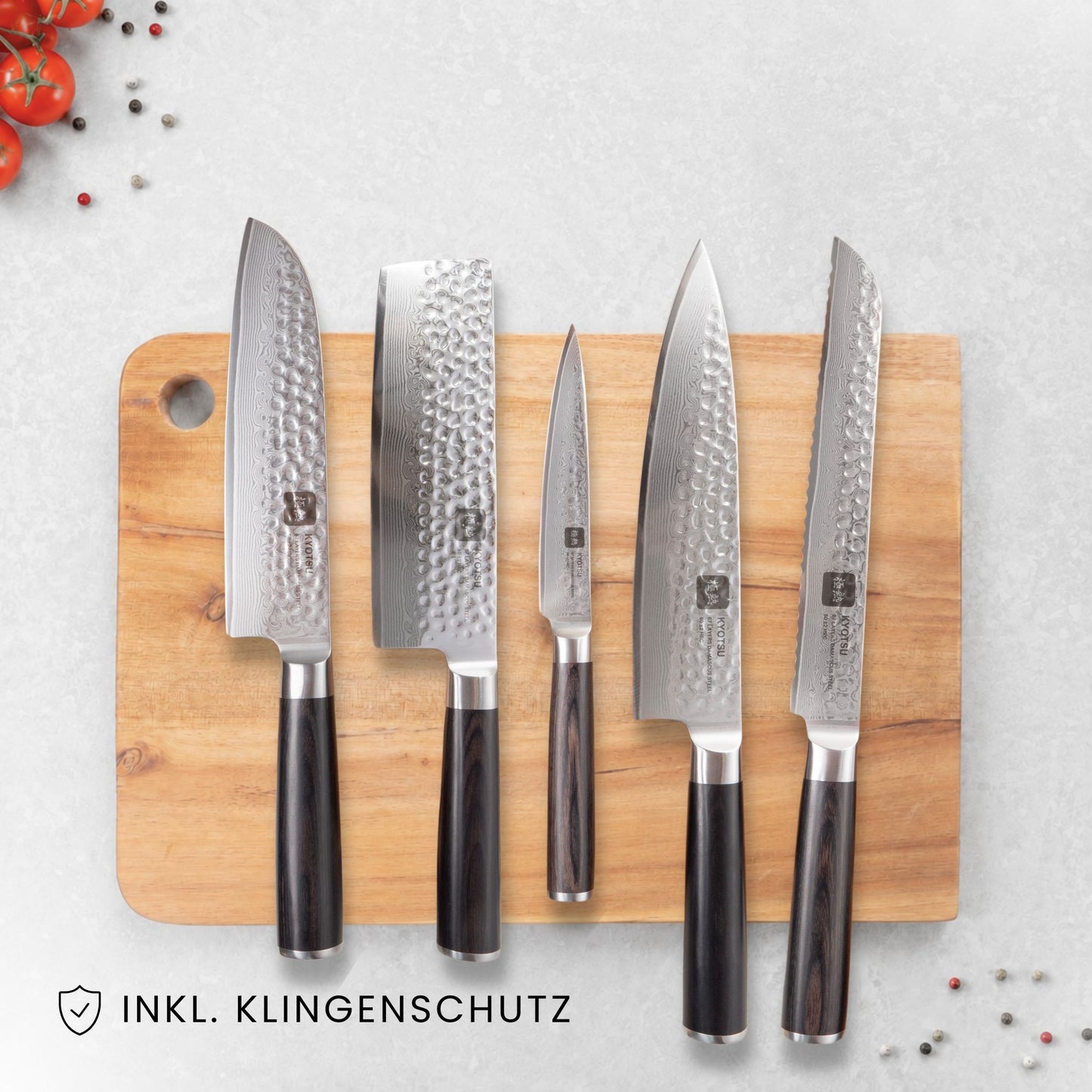 Kyotsu 5er-Set Pakka: Santoku-Messer, Nakiri-Messer, Allzweckmesser, Chefmesser und Brotmesser liegen auf einem Holz-Schneidebrett, daneben frische Zutaten.