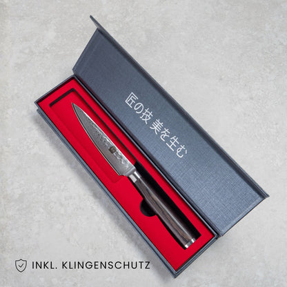 Kyotsu Allzweckmesser aus Damaststahl in geöffneter Verpackung, unten Links der Schriftzug "Inkl. Klingenschutz".