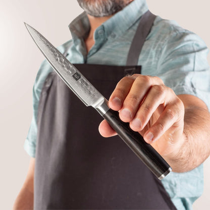 Person mit Schürze präsentiert Kyotsu Allzweckmesser aus Damaststahl.