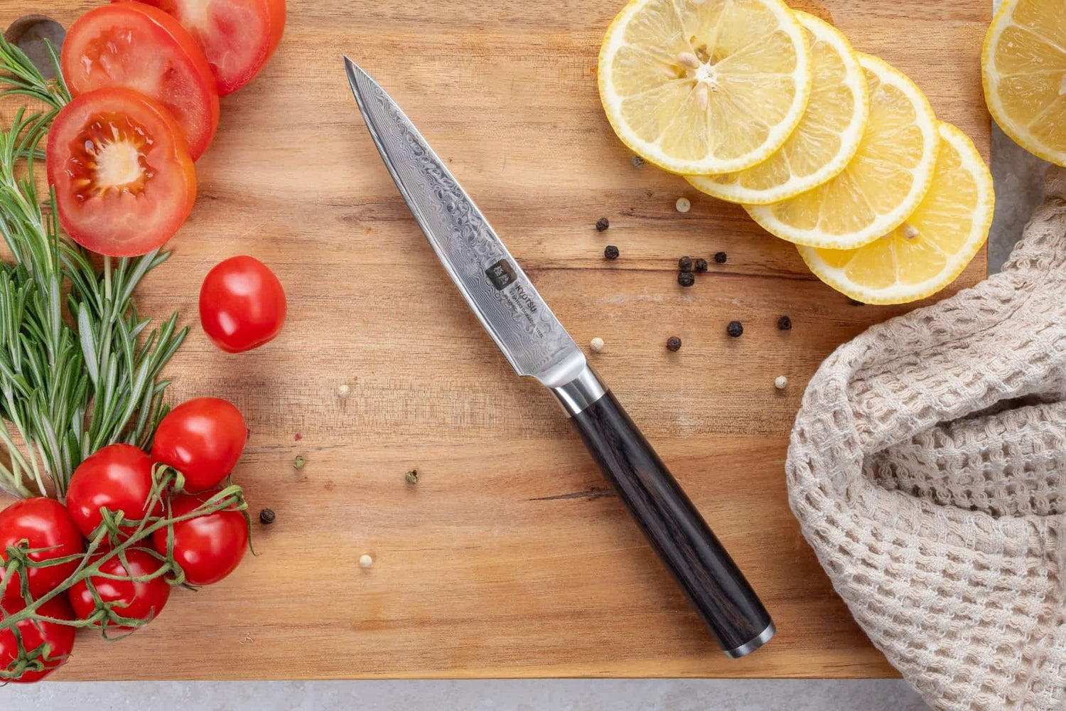 Kyotsu Allzweckmesser aus Damaststahl auf Holz-Schneidebrett mit frischen geschnittenen Zitronen und Tomaten – stilvolle Produktpräsentation für hochwertige Küchenmesser.
