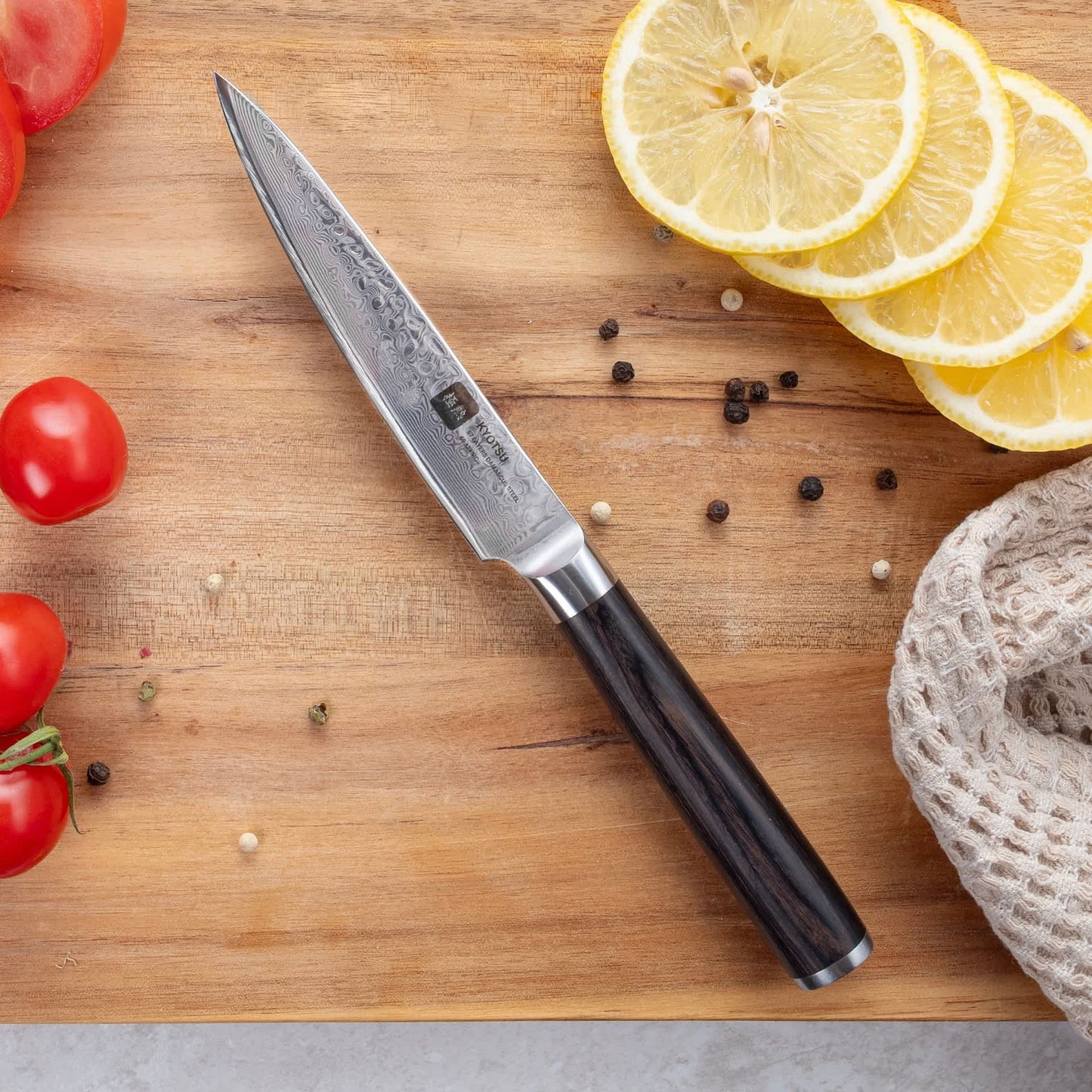 Kyotsu Allzweckmesser aus Damaststahl auf Holz-Schneidebrett mit frischen geschnittenen Zitronen und Tomaten – stilvolle Produktpräsentation für hochwertige Küchenmesser.