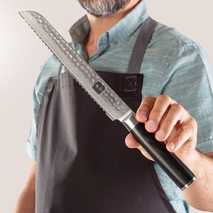 Person mit Schürze präsentiert Kyotsu Brotmesser aus Damaststahl.