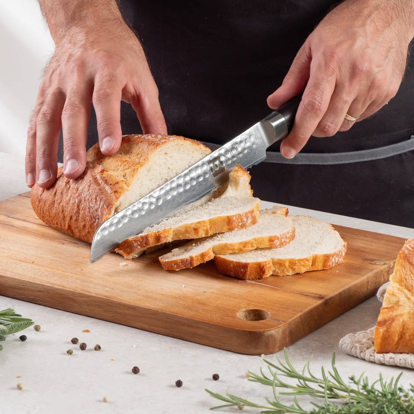 Eine Person schneidet mit dem Kyotsu Brotmesser aus Damaststahl ein Brot auf einem Holz-Schneidebrett – hochwertiges Messer in Aktion.