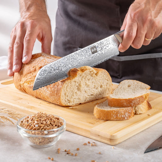 Eine Person schneidet mit dem Kyotsu Brotmesser aus Damaststahl ein Brot auf einem Holz-Schneidebrett – hochwertiges Messer in Aktion.
