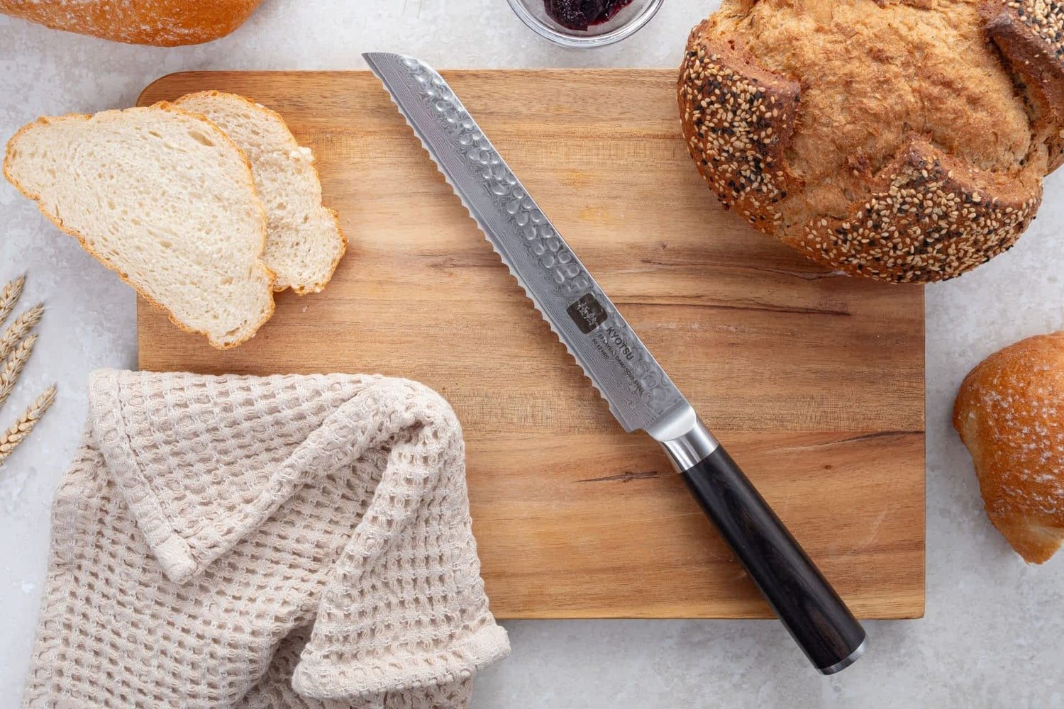 Kyotsu Brotmesser aus Damaststahl auf Holz-Schneidebrett mit frischem Brot – stilvolle Produktpräsentation für hochwertige Küchenmesser.