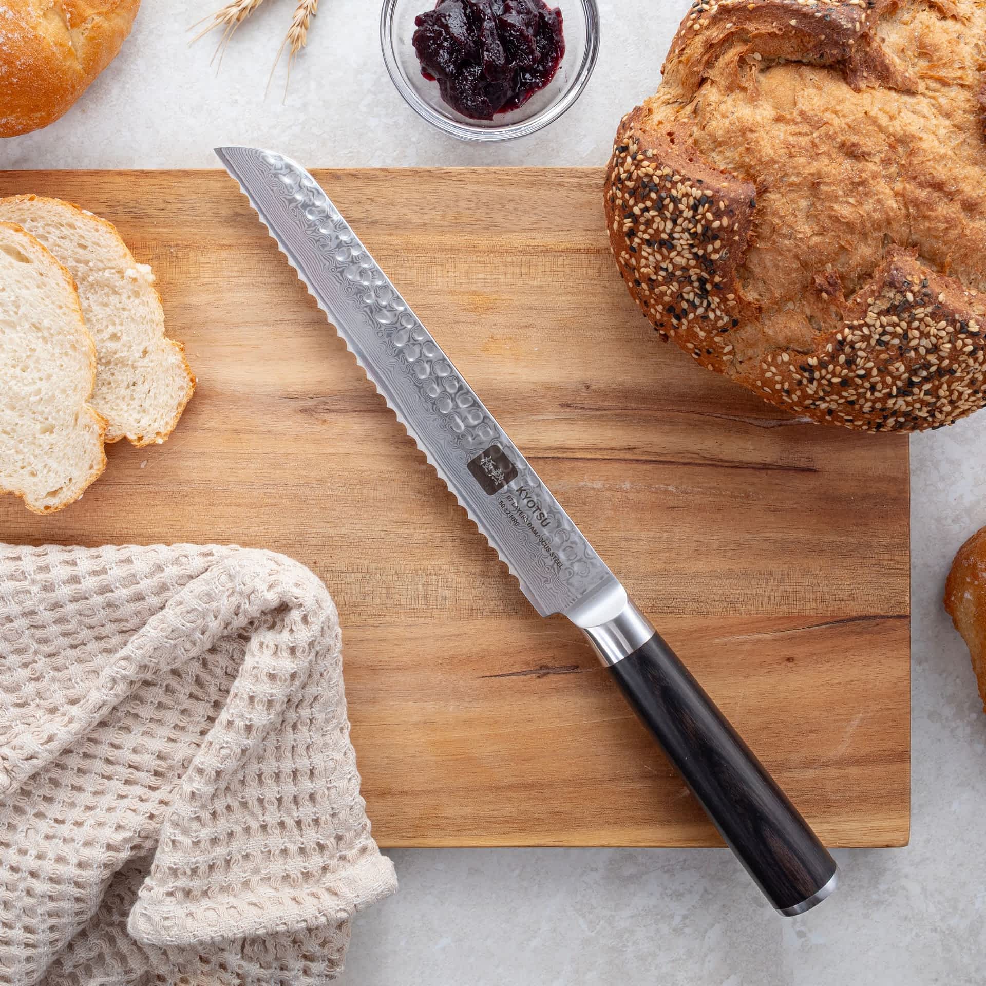 Kyotsu Brotmesser aus Damaststahl auf Holz-Schneidebrett mit frischem Brot – stilvolle Produktpräsentation für hochwertige Küchenmesser.