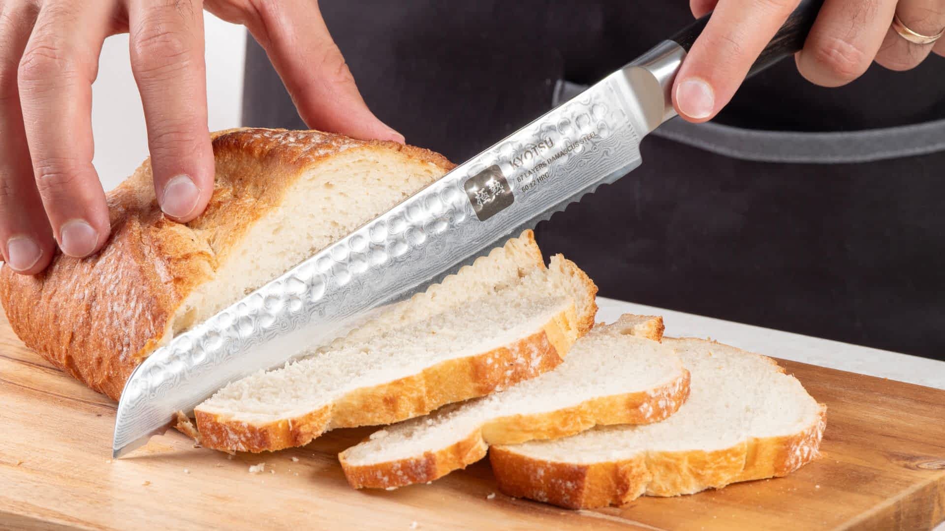 Eine Person schneidet mit dem Kyotsu Brotmesser aus Damaststahl ein Brot auf einem Holz-Schneidebrett – hochwertiges Messer in Aktion.