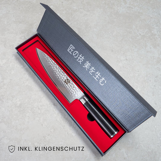 Kyotsu Chefmesser aus Damaststahl in geöffneter Verpackung, unten Links der Schriftzug "Inkl. Klingenschutz".