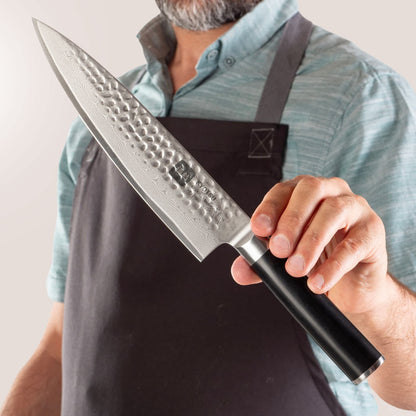 Person mit Schürze präsentiert Kyotsu Chefmesser aus Damaststahl.