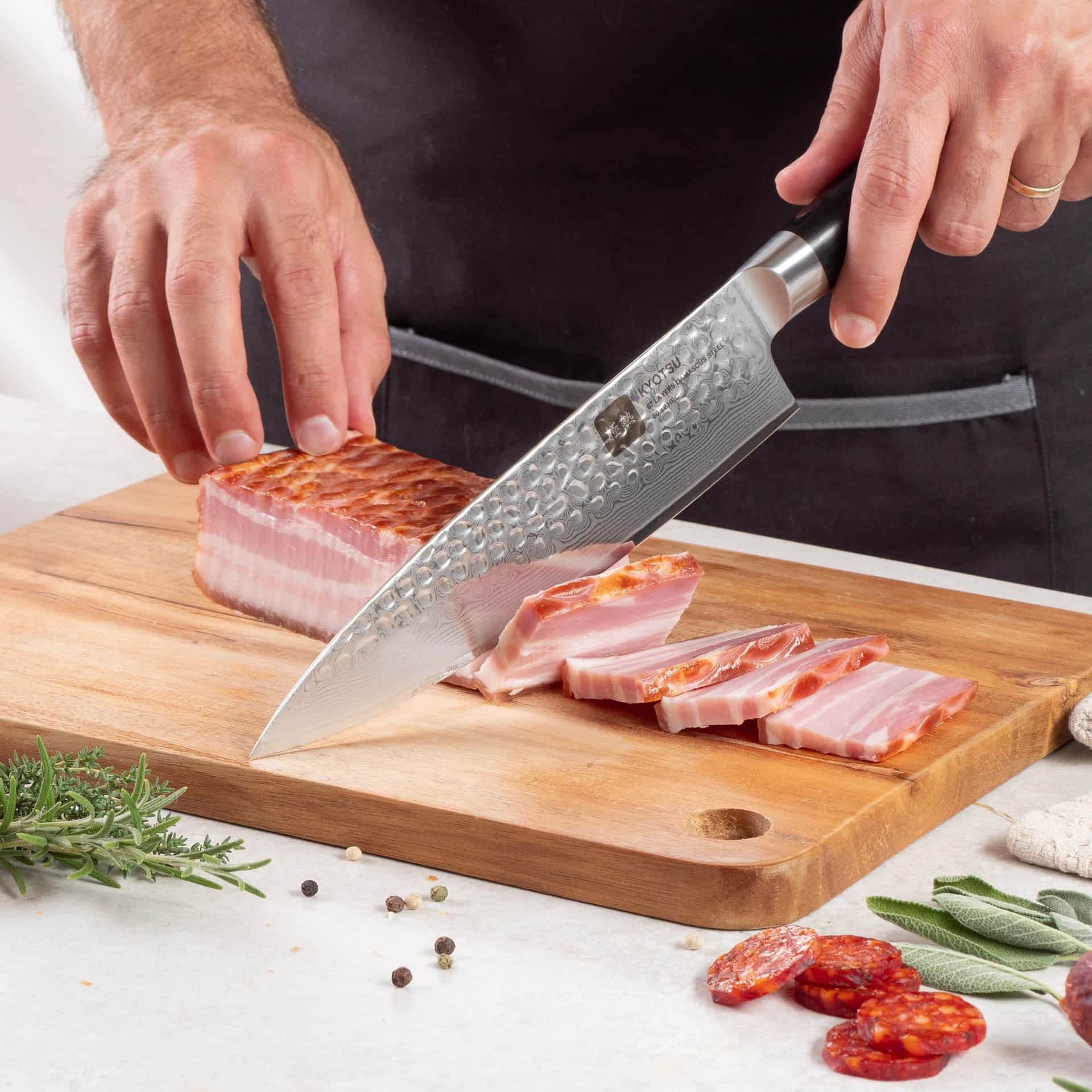 Eine Person schneidet mit dem Kyotsu Chefmesser aus Damaststahl Fleisch auf einem Holz-Schneidebrett – hochwertiges Messer in Aktion.