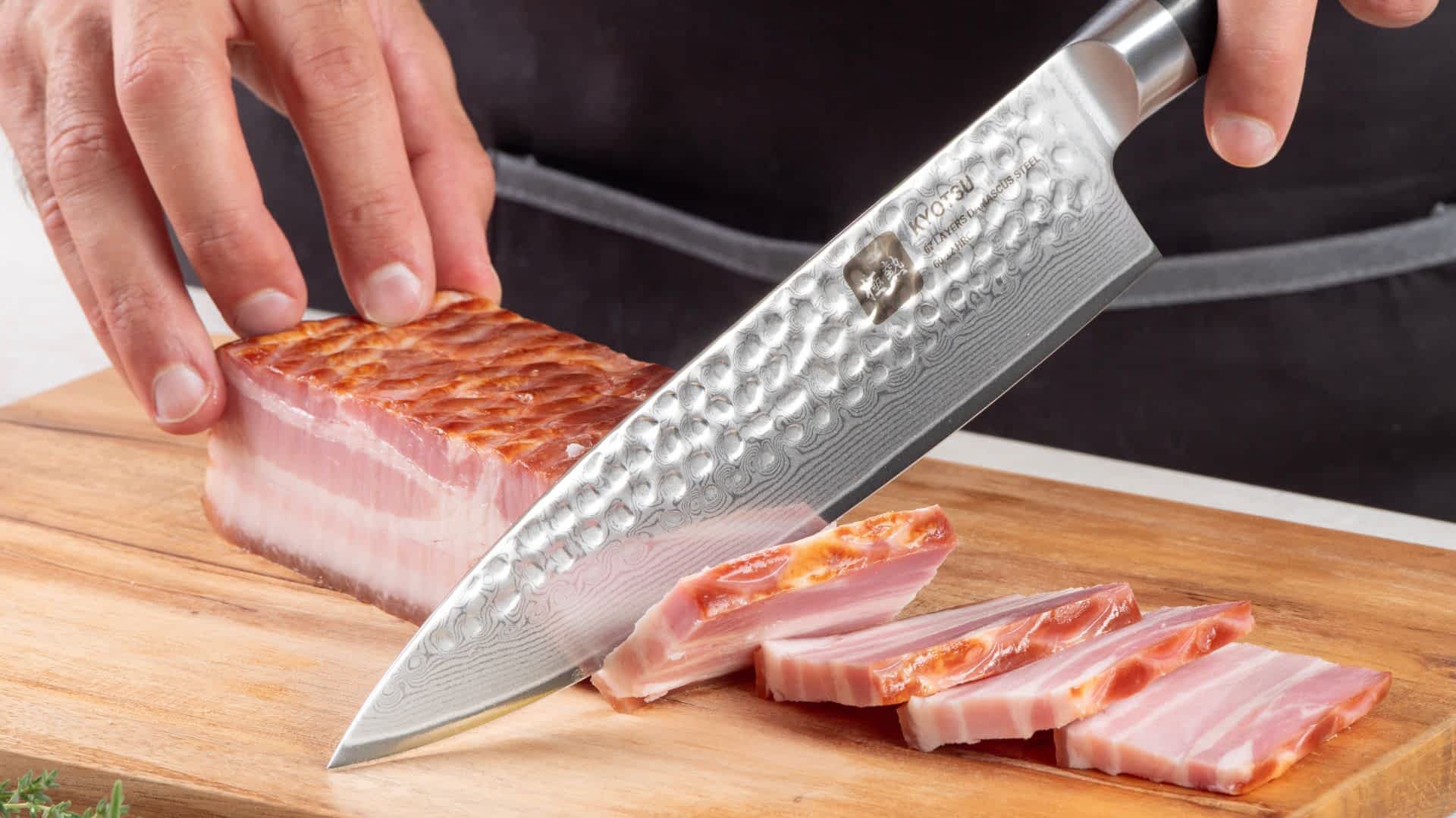 Eine Person schneidet mit dem Kyotsu Chefmesser aus Damaststahl Fleisch auf einem Holz-Schneidebrett – hochwertiges Messer in Aktion.