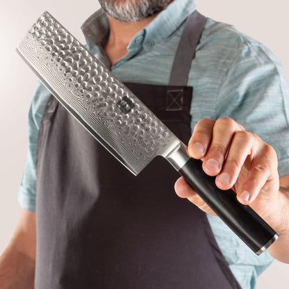 Person mit Schürze präsentiert Kyotsu Nakiri-Messer aus Damaststahl.