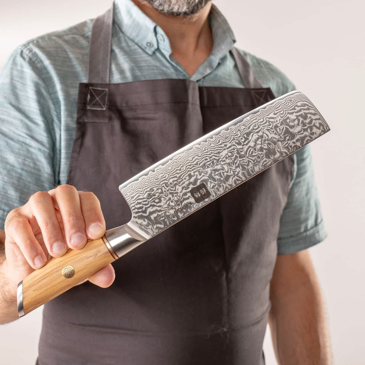 Person mit Schürze präsentiert Kyotsu Nakiri-Messer aus Damaststahl.