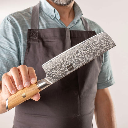 Person mit Schürze präsentiert Kyotsu Nakiri-Messer aus Damaststahl.