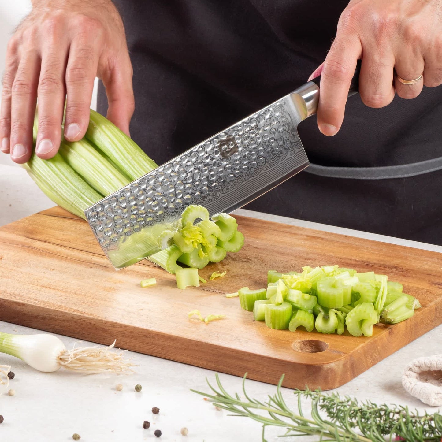Eine Person schneidet mit dem Kyotsu Nakiri-Messer aus Damaststahl Gemüse auf einem Holz-Schneidebrett – hochwertiges Messer in Aktion.