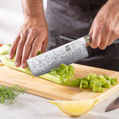 Eine Person schneidet mit dem Kyotsu Nakiri-Messer aus Damaststahl Gemüse auf einem Holz-Schneidebrett – hochwertiges Messer in Aktion.