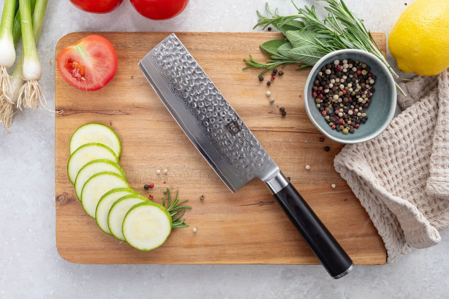 Kyotsu Nakiri-Messer aus Damaststahl auf Holz-Schneidebrett mit frischen Zucchini und Tomaten – stilvolle Produktpräsentation für hochwertige Küchenmesser.