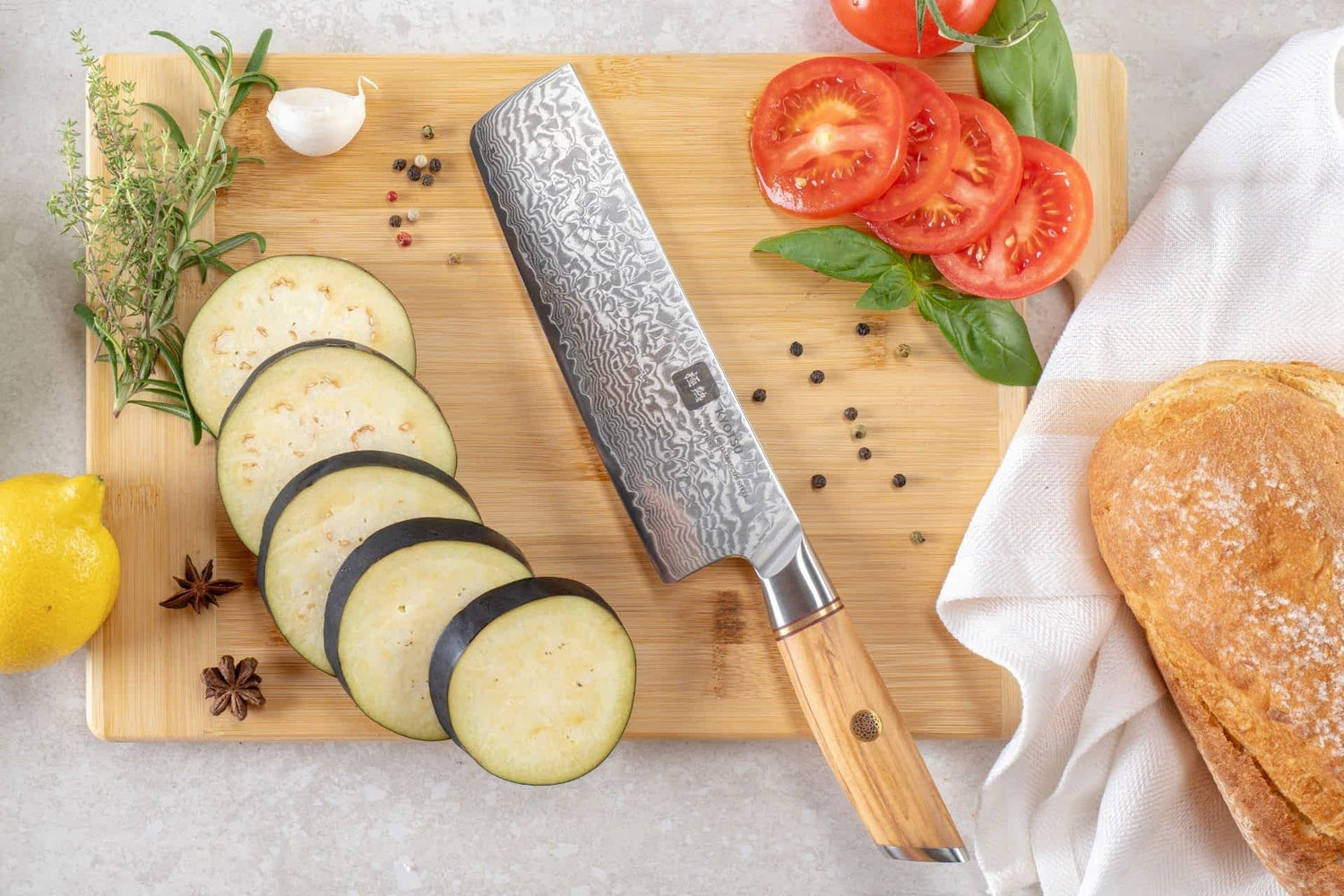 Kyotsu Nakiri-Messer aus Damaststahl auf Holz-Schneidebrett mit frischen Auberginen und Tomaten – stilvolle Produktpräsentation für hochwertige Küchenmesser.