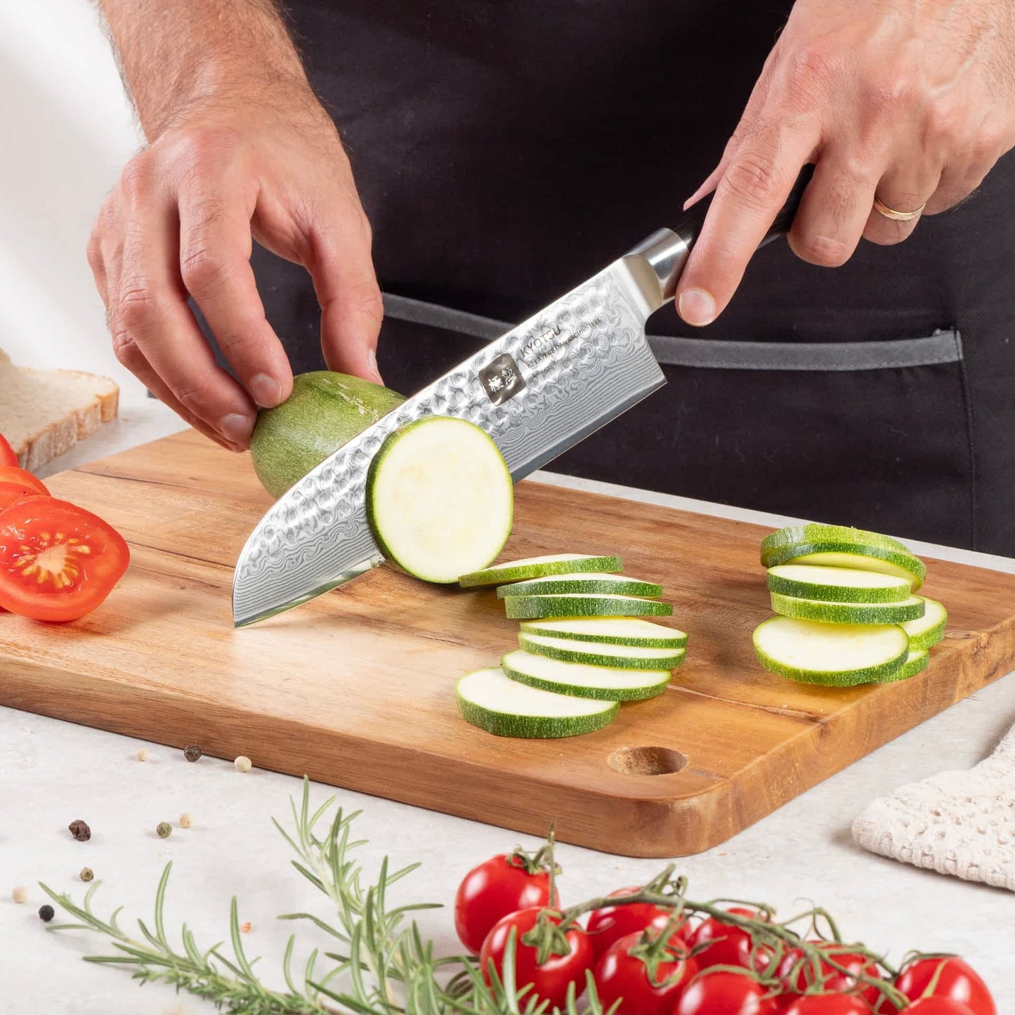 Eine Person schneidet mit dem Kyotsu Santoku-Messer aus Damaststahl Zucchini auf einem Holz-Schneidebrett – hochwertiges Messer in Aktion.