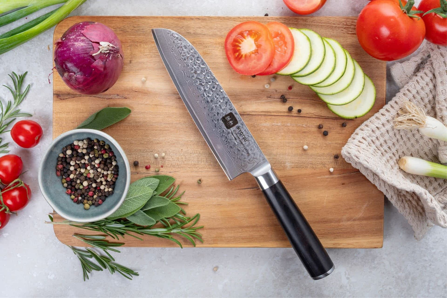 Kyotsu Santoku-Messer aus Damaststahl auf Holz-Schneidebrett mit frischen Zutaten – stilvolle Produktpräsentation für hochwertige Küchenmesser.