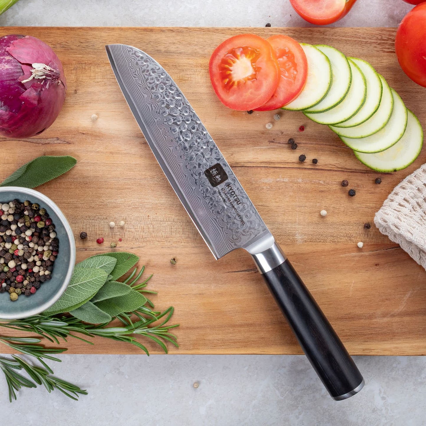 Kyotsu Santoku-Messer aus Damaststahl auf Holz-Schneidebrett mit frischen Zutaten – stilvolle Produktpräsentation für hochwertige Küchenmesser.