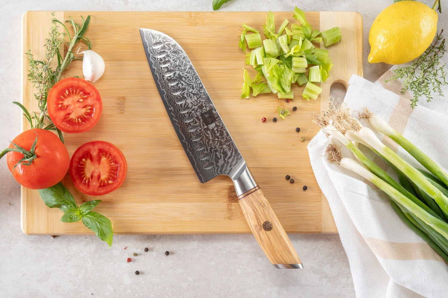 Kyotsu Santoku-Messer aus Damaststahl auf Holz-Schneidebrett mit frischen Zutaten – stilvolle Produktpräsentation für hochwertige Küchenmesser.