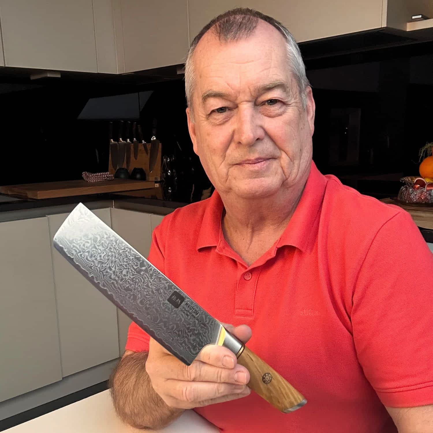 Ein Mann zeigt mit einem Lächeln im Gesicht das Nakiri-Messer von Kyotsu in die Kamera.