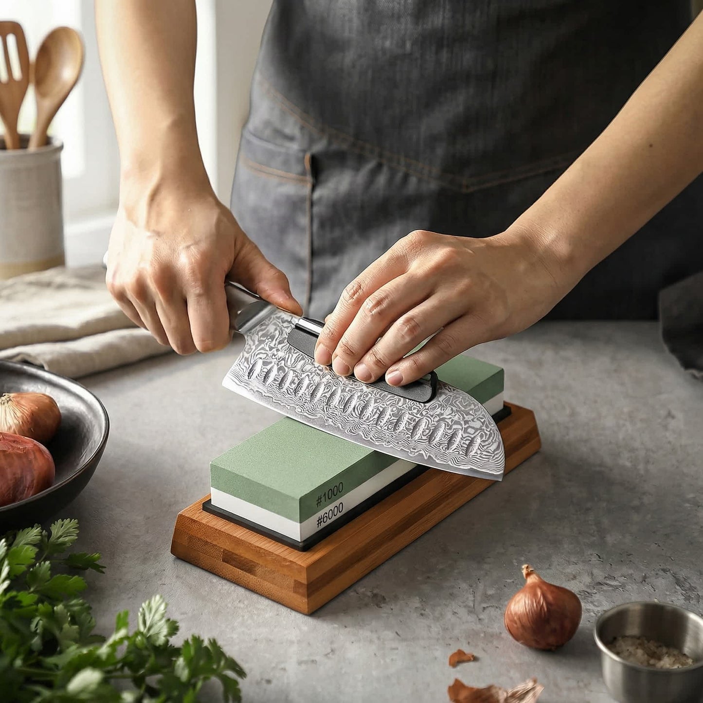 Eine Person schärft mit dem Kyotsu Schleifstein-Set ein Messer in der Küche. Daneben liegen Zwiebeln, Kräuter etc.