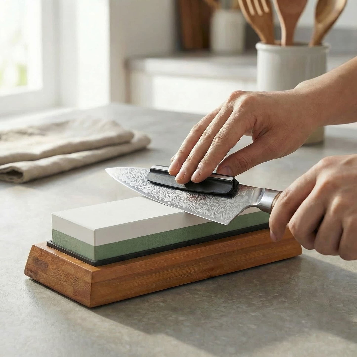 Eine Person schleift mit dem Kyotsu Schleifstein-Set inkl. Bambushalterung und Winkelführung ein Damastmesser in einer Küche.